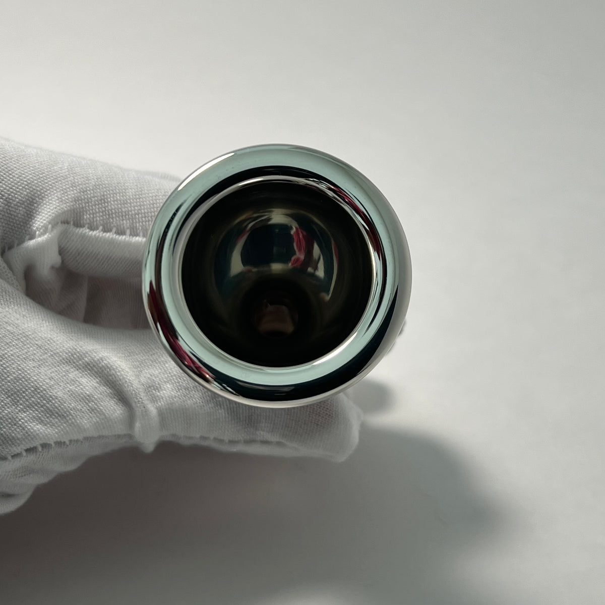 Tuba mouthpiece held by a gloved hand on a neutral background