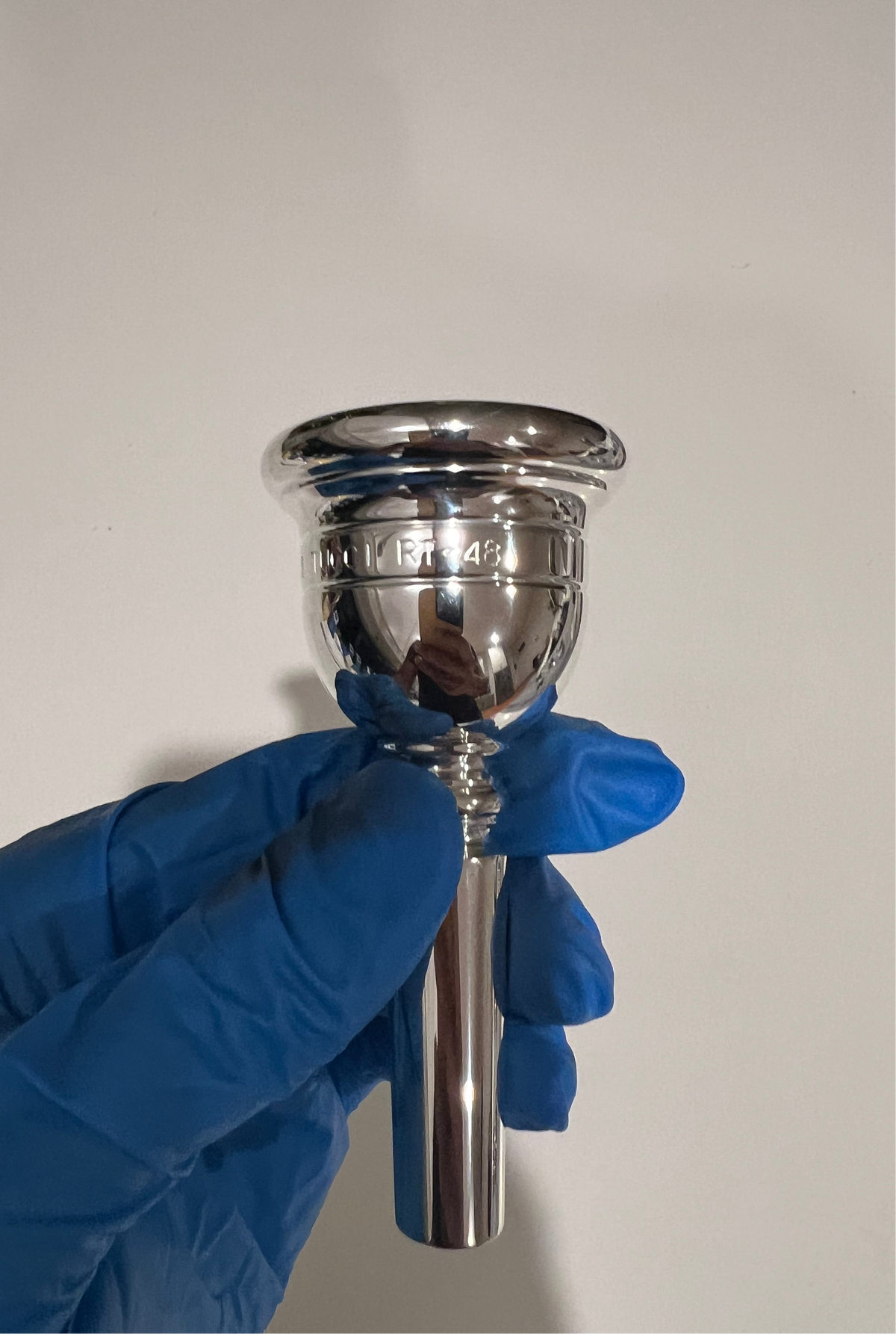 Silver Robert Tucci RT-48 Tuba Mouthpiece being held in hand with blue glove.