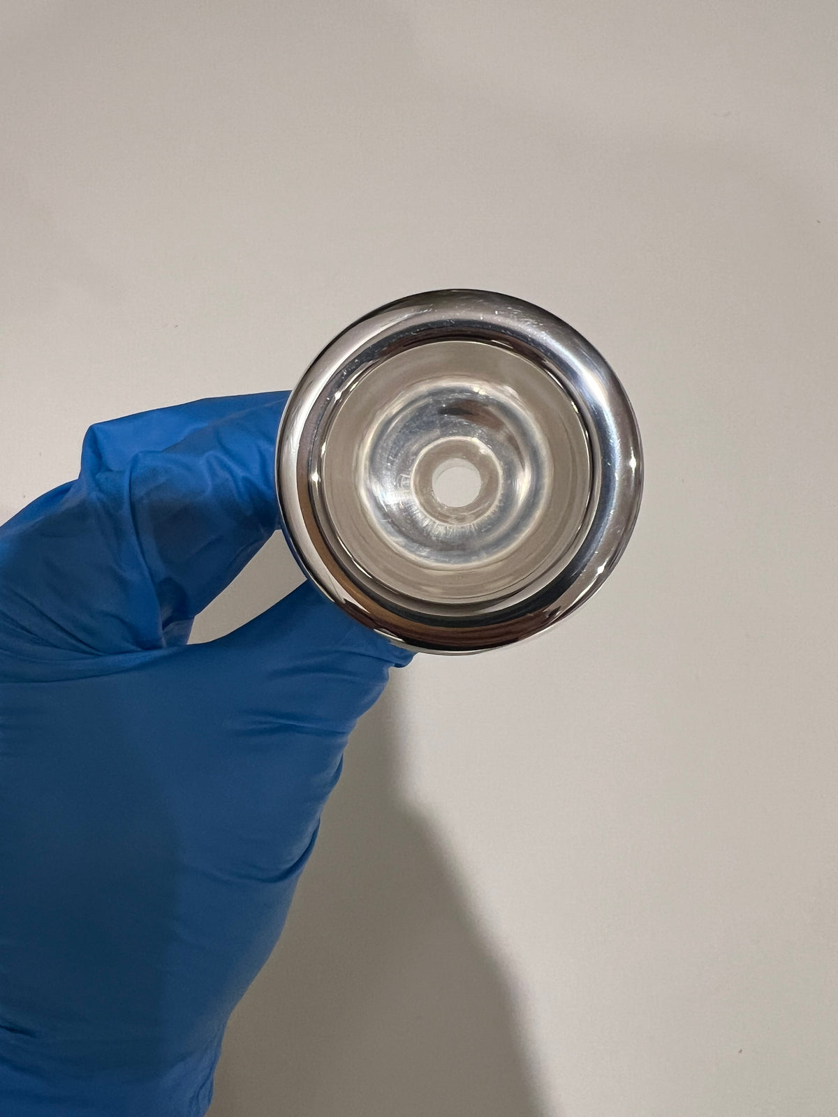 Silver Robert Tucci RT-48 Tuba Mouthpiece being held in hand with blue glove.