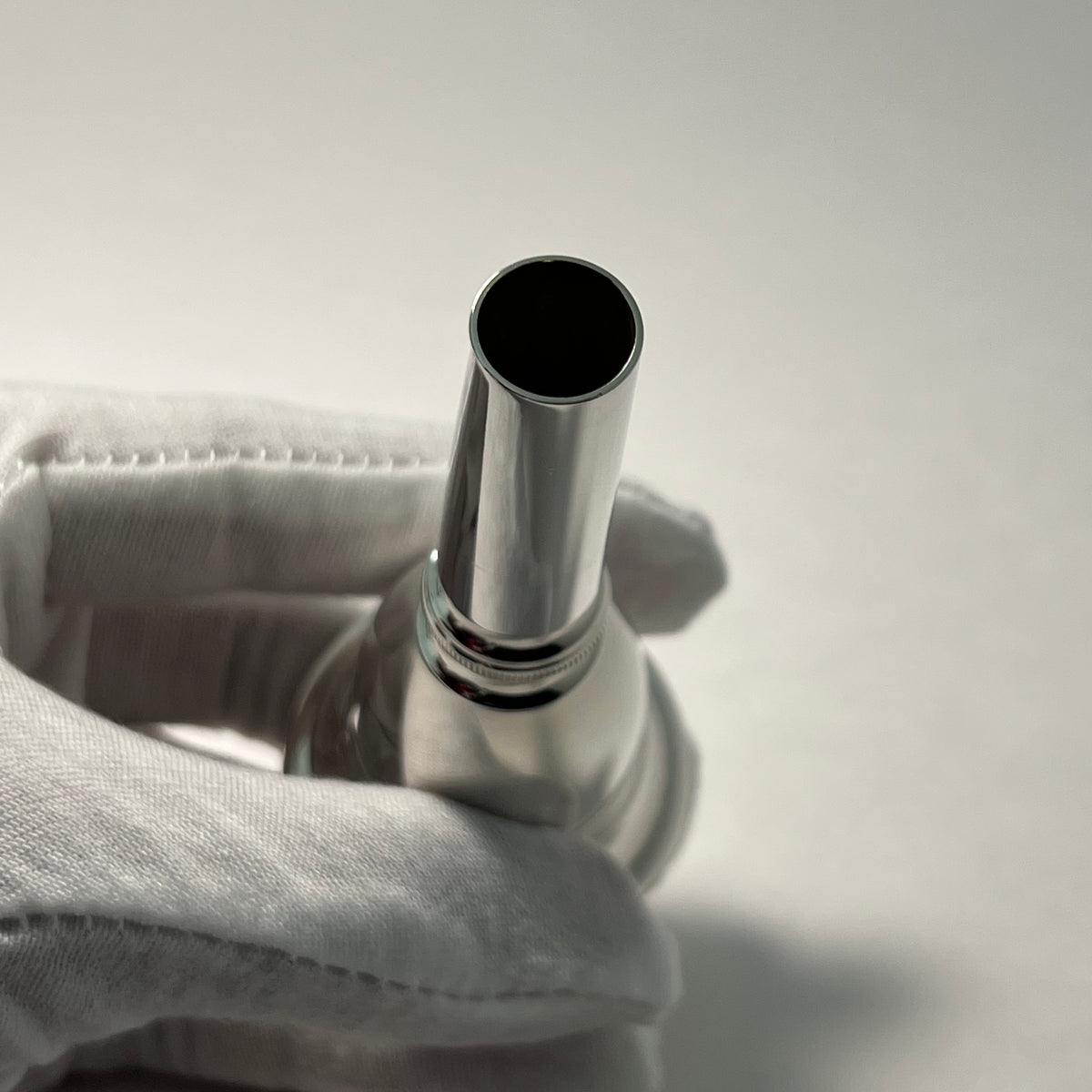 Tuba mouthpiece shank held by a gloved hand against a neutral background