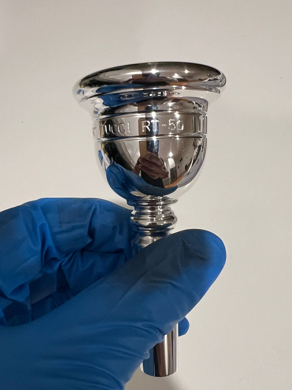 Silver tuba mouthpiece on a white background being held in hand with blue glove