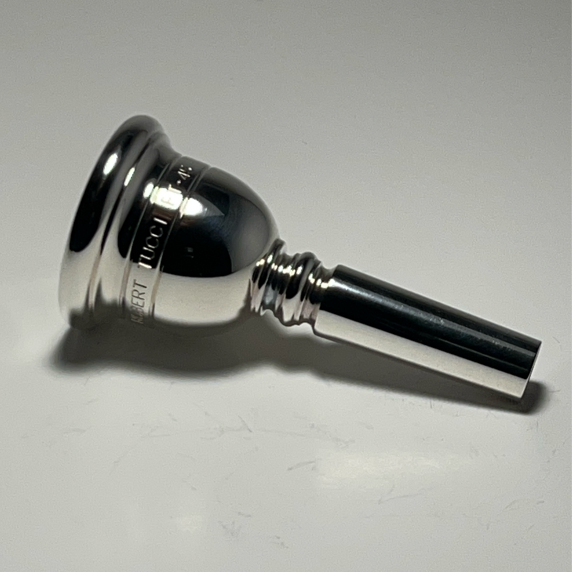 Silver Rober Tucci Tuba Mouthpiece with Blue Box with "Robert Tucci Mouthpieces" Printed on the side.