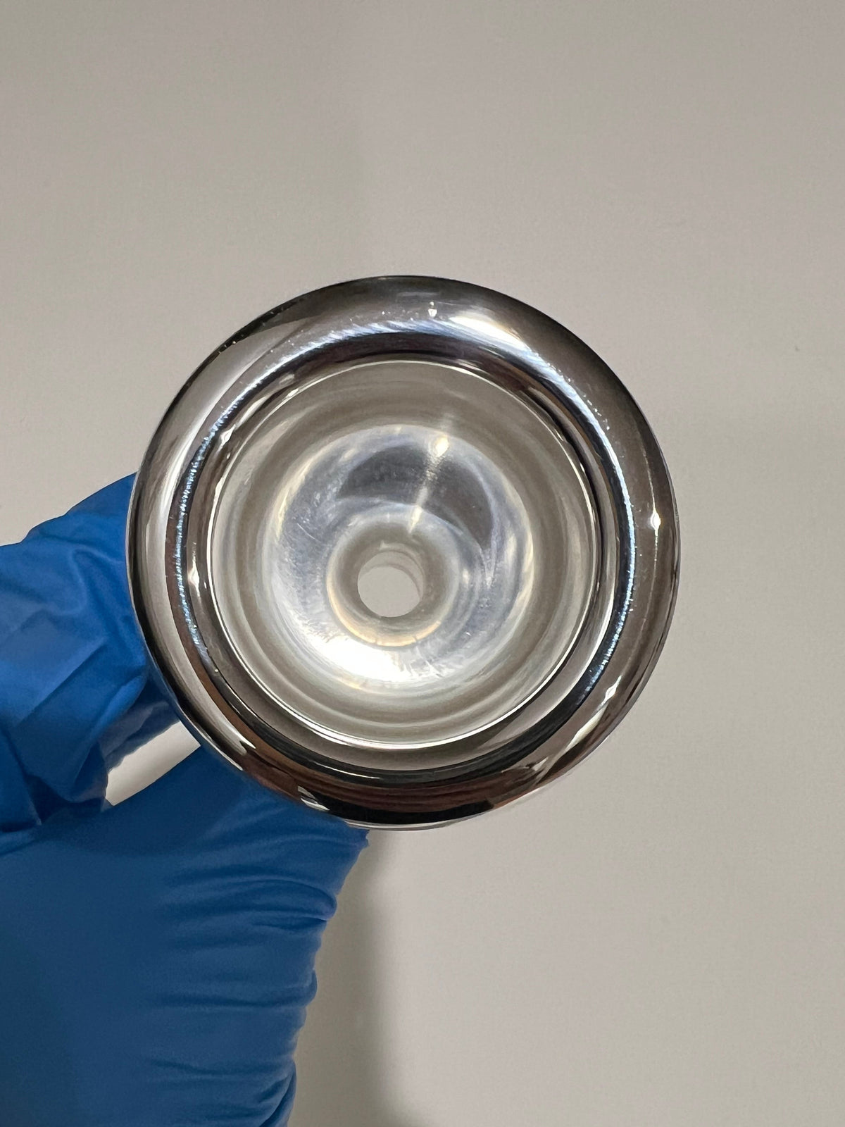 Silver tuba mouthpiece on a white background being held in hand with blue glove