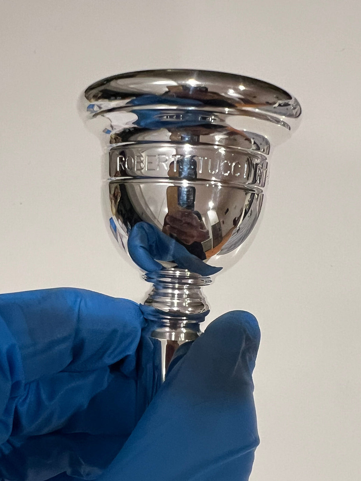 Silver tuba mouthpiece on a white background being held in hand with blue glove