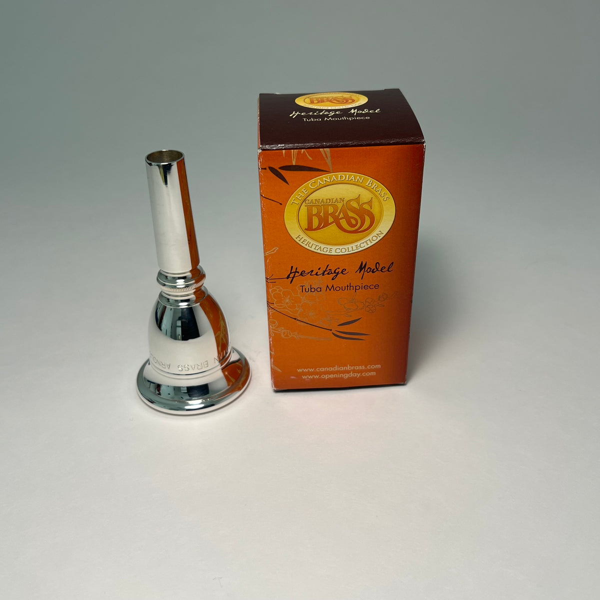 Silver tuba mouthpiece and its packaging on a gray background