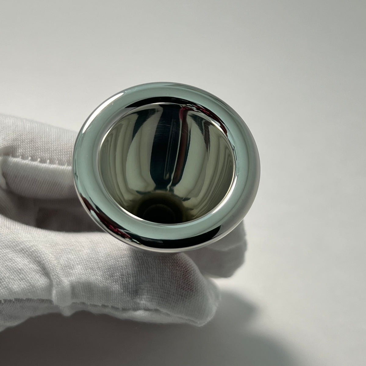 Tuba mouthpiece rim held by a gloved hand on a light gray background