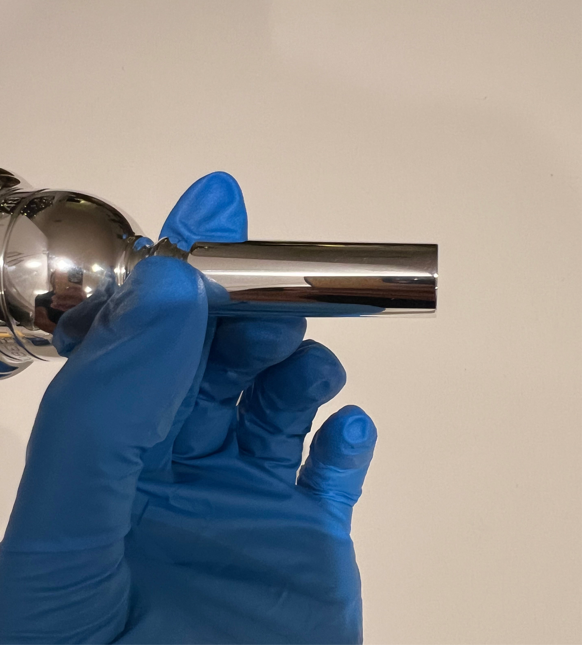 Silver Robert Tucci RT-48 Tuba Mouthpiece being held in hand with blue glove.