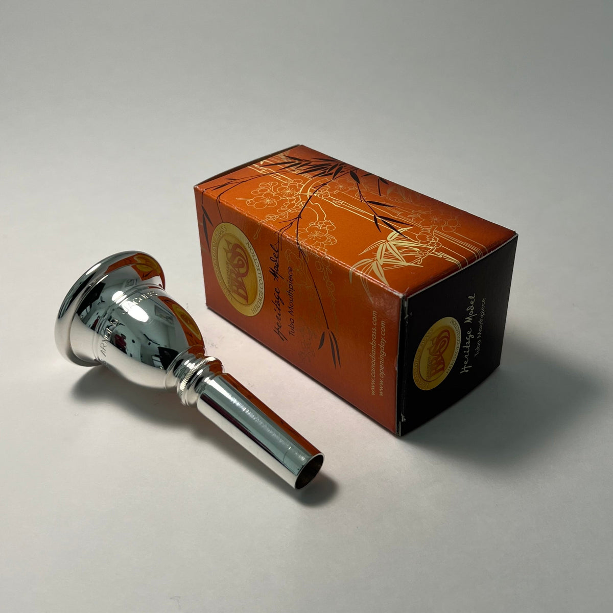 Silver tuba mouthpiece with packaging on a gray background